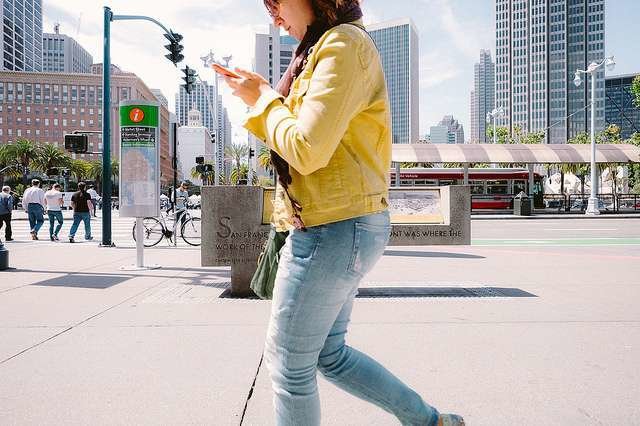 Una mujer camina por la calle usando su teléfono móvil. (Sonny Abesamis, Flickr)
