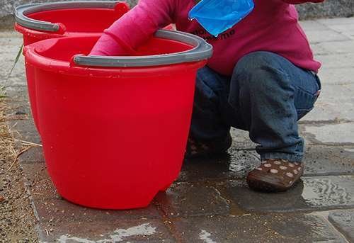 Una niña juega con un cubo de agua.