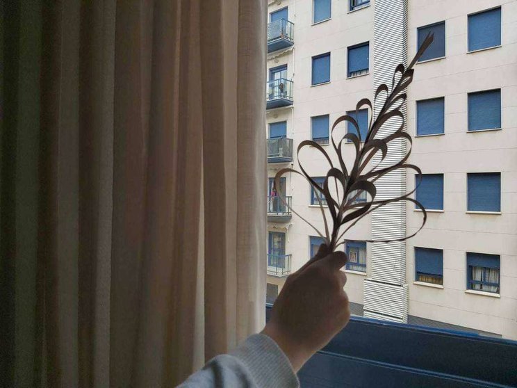 Un niño muestra por la ventana una palma elaborada con cartulina. (EL CORREO)