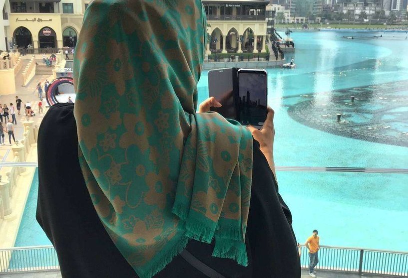Una mujer musulmana toma imágenes de la fuente situada ante el Burj Khalifa en Dubai. (EL CORREO)