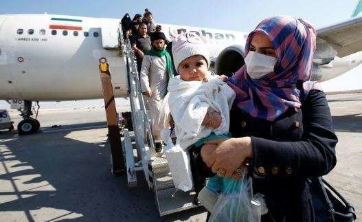 Una madre protegida con mascarilla baja de un avión iraní. (Reuters)